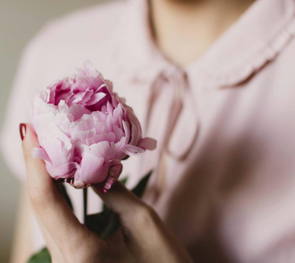 Close-up of a woman gently holding a pink peony flower, showcasing softness and elegance.